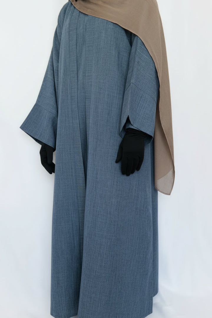 Person wearing a long blue garment with a beige headscarf on a white background