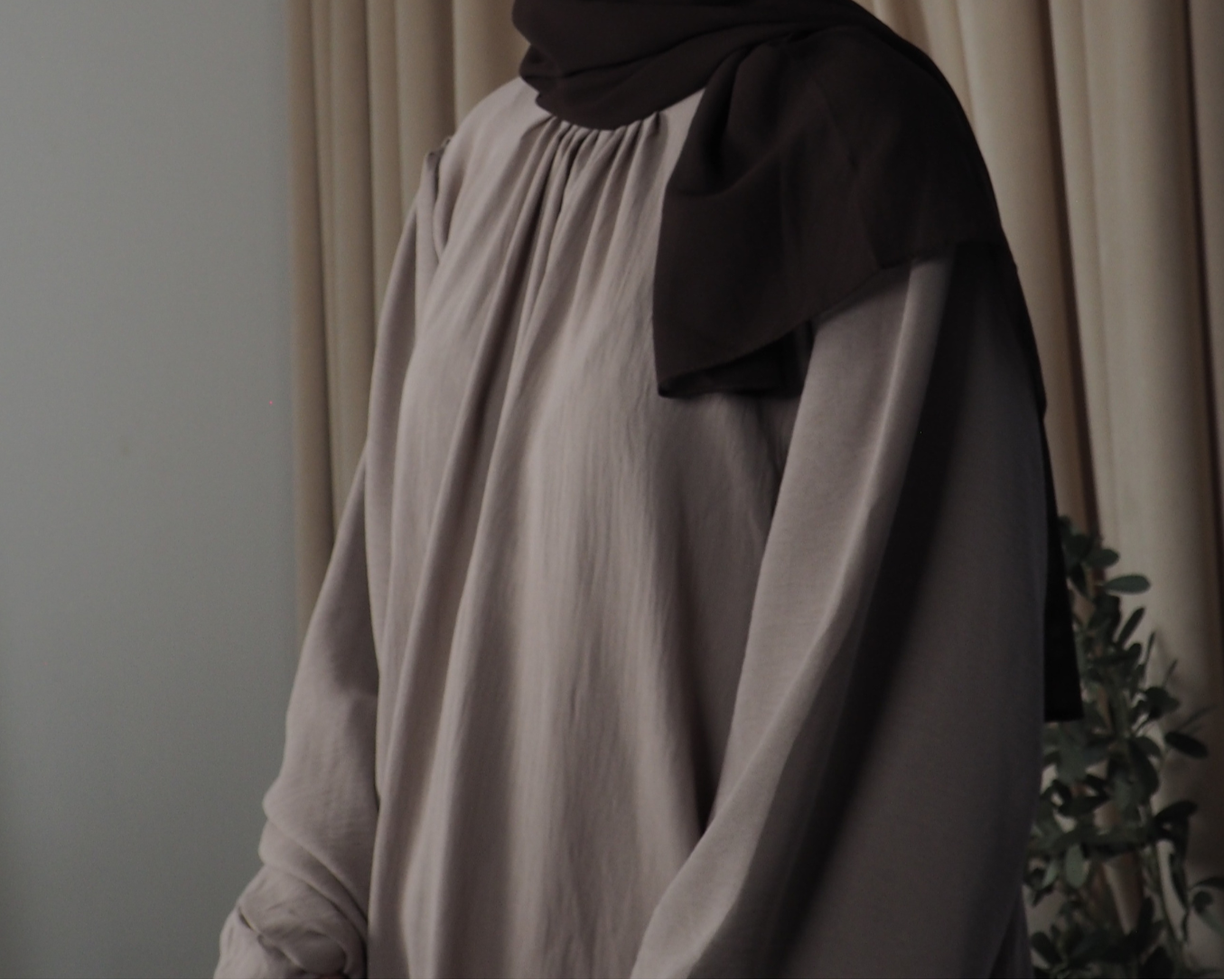 A person wearing a lilac grey abaya with balloon sleeves and pleated details, paired with a black headscarf.