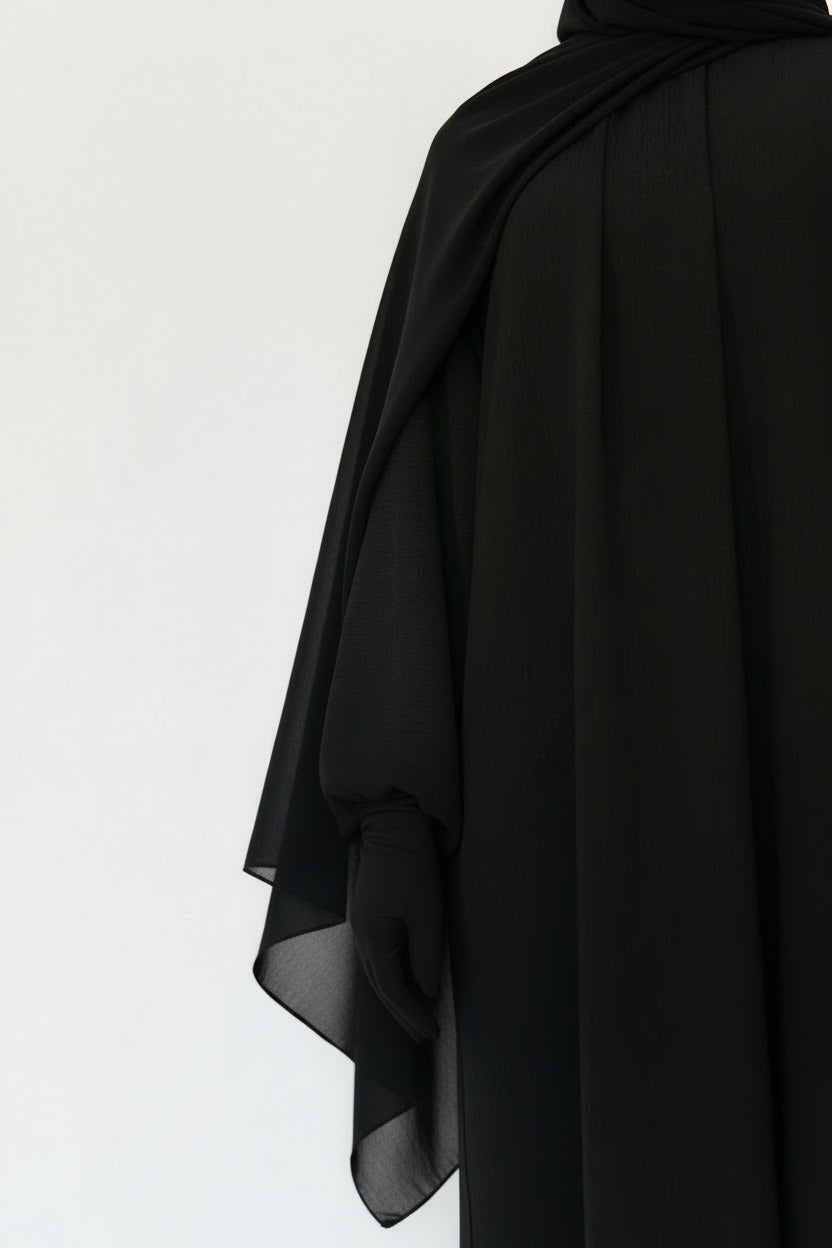 Black abaya worn by a person on a white background