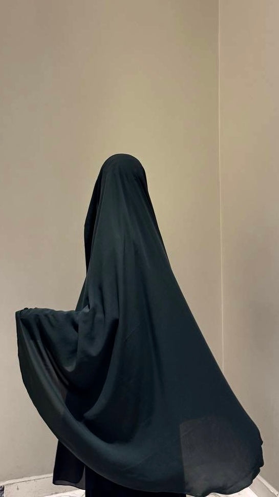 Person wearing a black burqa against a plain background