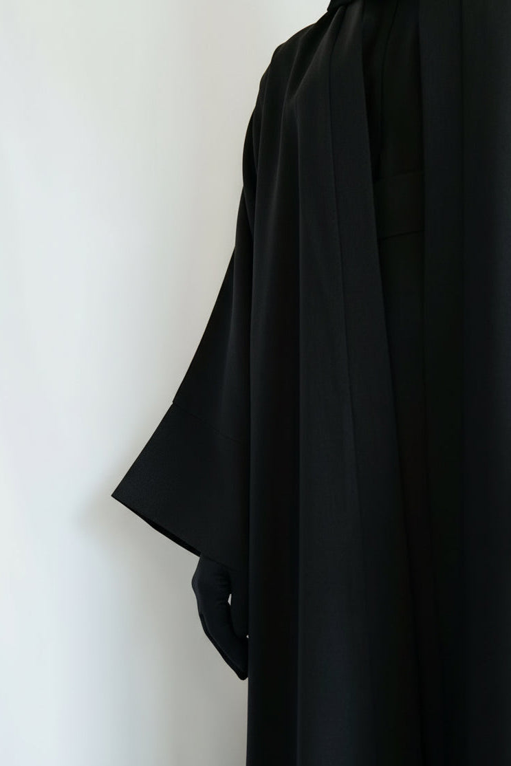 Black abaya worn by a person against a white background