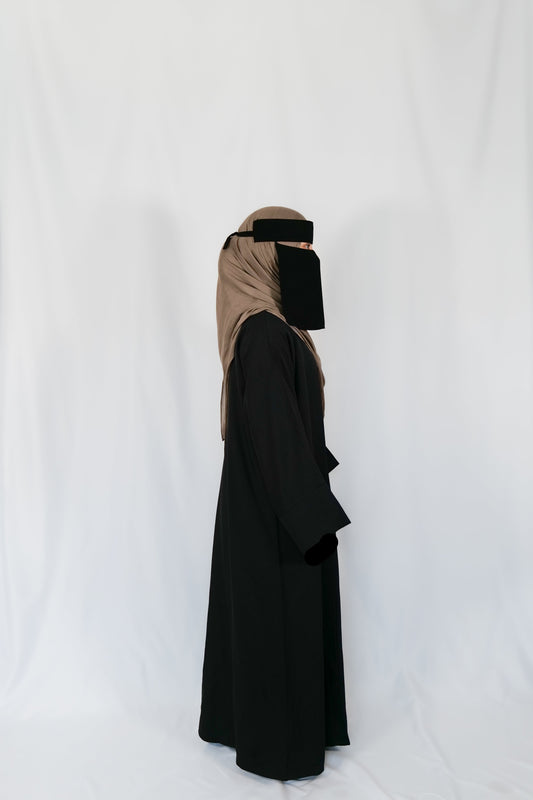 Person wearing a black abaya with a beige headscarf on a white background
