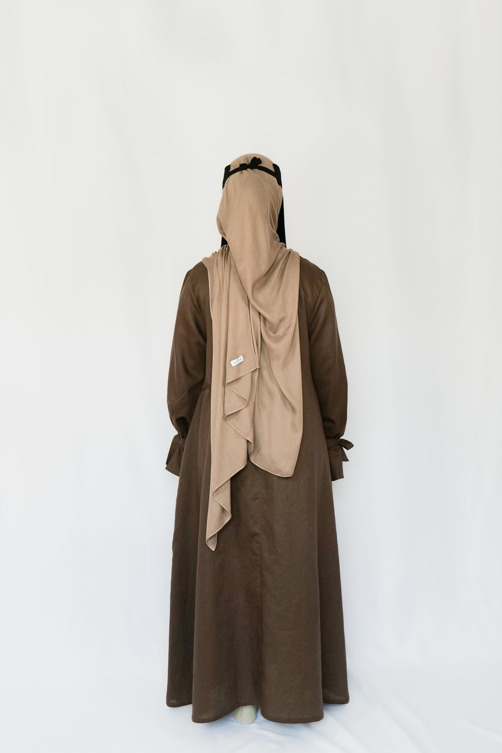 Person wearing a brown abaya with a beige hijab on a white background