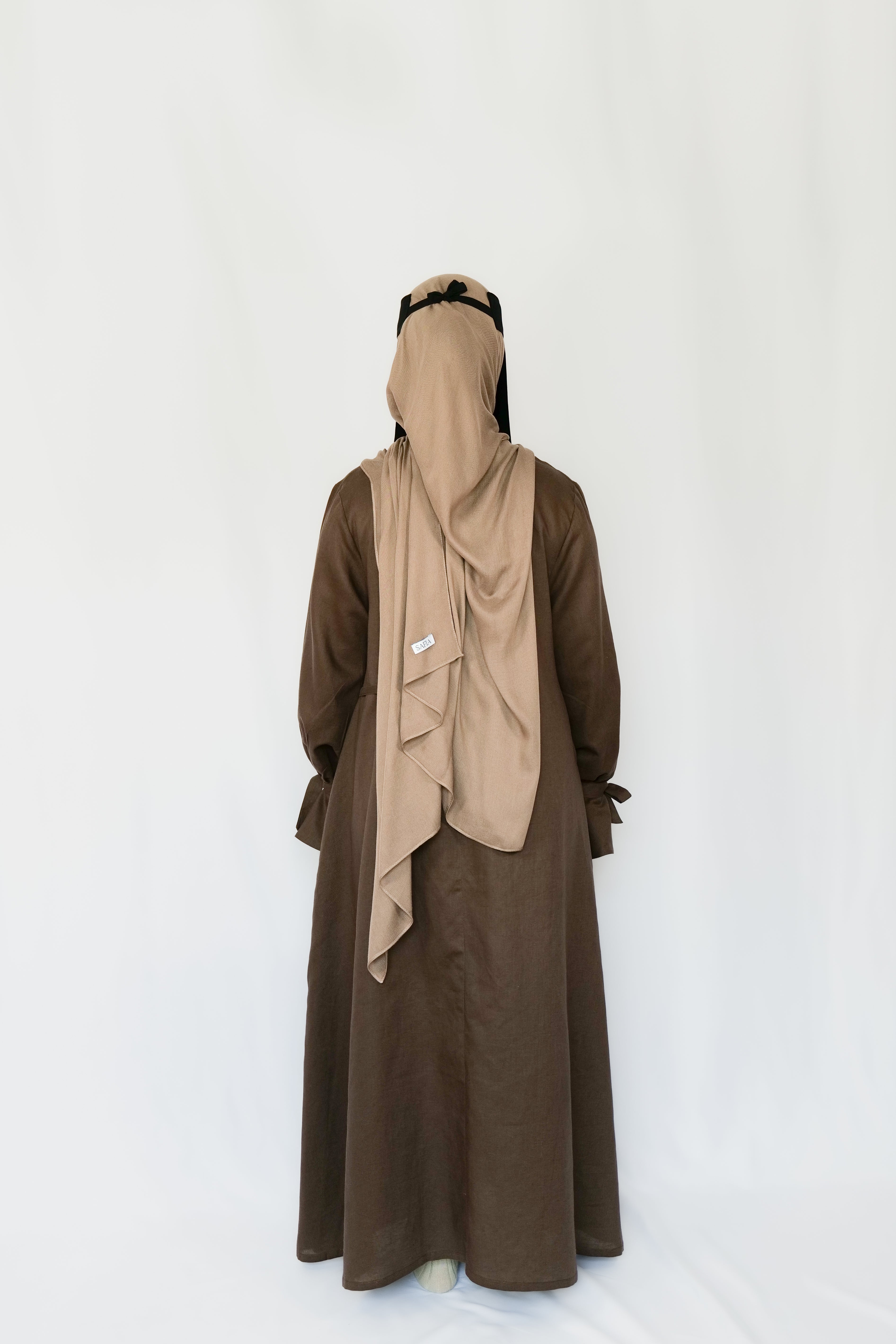 Person wearing a brown abaya with a beige hijab on a white background