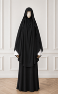 Black abaya worn by a mannequin against a white paneled wall.